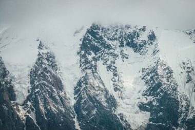 Atmosferik dağlar alçak bulutlarda kar kornişleri olan büyük karlı dağ tepeleriyle kaplı. Bulutlu havada kar beyazı yüksek zirvesiyle muhteşem bir manzara. Bulutlardaki dev dağ duvarı.