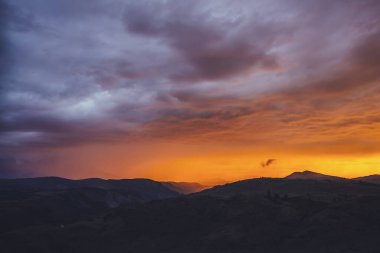 Atmosferik manzara. Dağların siluetleriyle. Ağaçların arka planında parlak turuncu mavi şafak gökyüzü. Günbatımının ya da aydınlatıcı rengin gün doğumunun olduğu renkli doğa manzarası. Günbatımı ödemesi