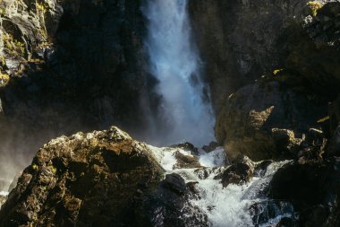 Atmosferik minimumda kaya duvarında dikey büyük şelale var. Karanlık vadide güçlü bir şelale. Islak kayaların üzerine düşen yüksek türbülanslı su akışının doğal arka planı.
