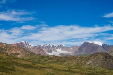 Atmosferik dağ manzarası, büyük güzel buzullar ve mavi bulutlu gökyüzünün altında keskin kayalar. Büyük bir buzul diline sahip manzaralı dağ manzarası. Yeşil dağ geçidinden kahverengi kayalara müthiş bir manzara..