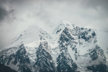 Atmosferik dağlar alçak bulutlarda kar kornişleri olan büyük karlı dağ tepeleriyle kaplı. Bulutlu havada kar beyazı yüksek zirvesiyle muhteşem bir manzara. Bulutlardaki dev dağ duvarı.