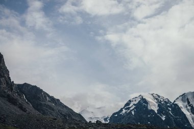 Bulutlu gökyüzünde harika karlı dağ manzarası. Atmosferik bulutlu, yüksek dağlı ve buzullu bir manzara. Alçak bulutlarda karlı büyük dağlar. Güzel karlı dağlar.