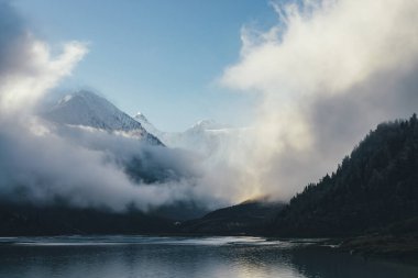Yoğun bulutların üzerindeki kar kaplı dağların güzel manzarası. Mavi gökyüzündeki yoğun alçak bulutlar arasında beyaz kar zirvesi olan manzaralı dağ manzarası. Karlı zirvesi olan harika bir dağ manzarası.