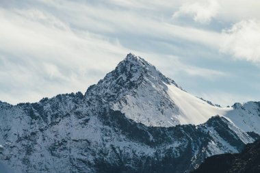 Gökyüzündeki sirrus bulutlarının altında zirveye ulaşmış yüksek karlı dağ duvarına harika bir manzara. Alp manzarası, büyük karla kaplı dağlarla güneş altında keskin bir tepe noktası. Beyaz karlı, sivri uçlu güneş ışığı.
