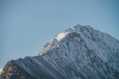 Minimalist güneşli dağ manzarası, karla kaplı dağ tepesi, açık mavi gökyüzünde altın güneş ışığı. Yüksek karlı gün ışığında tepe noktası olan minimum alp manzarası. Sivri tepelerde keskin kayalar üzerinde kar