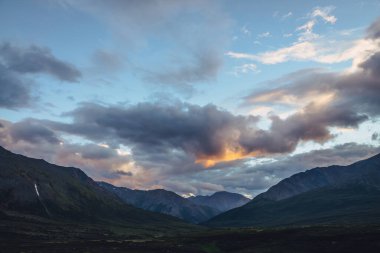 Bulutlu gökyüzünde altın şafak ışığıyla güzel bir dağ manzarası. Gün batımı gökyüzünde aydınlatıcı renklere sahip manzaralı dağ manzarası. Gün doğumunda dağların siluetleri. Gökyüzünde aydınlatan altın rengi güneş ışığı