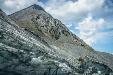Güneşli bir günde büyük bir buzulun ve piramit şeklinde yüksek bir dağın zirvesinin olduğu manzaralı dağlık bir arazi. Büyük taşları ve zirvesi olan buzlu tepeli muhteşem bir dağ manzarası. Buzul ve taşlar güneş ışığında