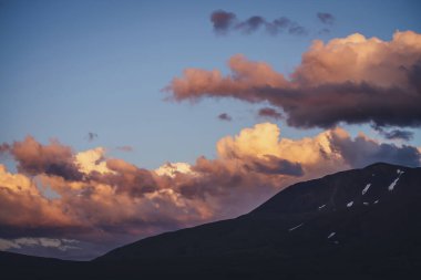 Atmosferik dağ manzarası, şafak vakti leylak rengi gökyüzü. Dağlarda gün batımını aydınlatan manzaralı bir manzara. Dağlarda, pastel tonlarda güzel bir gündoğumu. Şafak vakti bulutlu gökyüzünde aydınlatıcı bir renk.