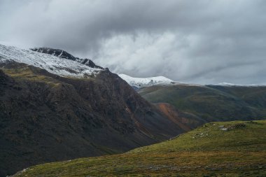 Atmosferik alp manzarası derin vadi ve karla kaplı çok renkli dağlarla bulutlu havada. Bulutlu gökyüzünün altında karla kaplı sıradağlarla güzel bir manzara. Karlı Motley yüksek dağları
