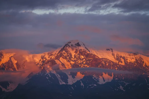 低雲の中で夜明けの太陽に照らされた素晴らしい雪の山々と風景山の風景 日没時や日の出時に高い山の頂点を持つ素晴らしい高山風景 オレンジの光の上にある大きな氷河 — ストック写真