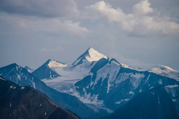 曇り空の下で青い白い色で大きな雪の山の頂点と素晴らしい山の風景 白い雲の下で雪と指摘トップと高い山の壁と大気高地の風景 — ストック写真