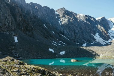 Karlı dağ, buzul gölünün berrak sularına yansıyor. Berrak gökyüzünün altındaki dağ gölünün su yüzeyinde buzul yansıması olan güzel güneşli bir manzara. Dağdaki gölde yansıyan karlar..