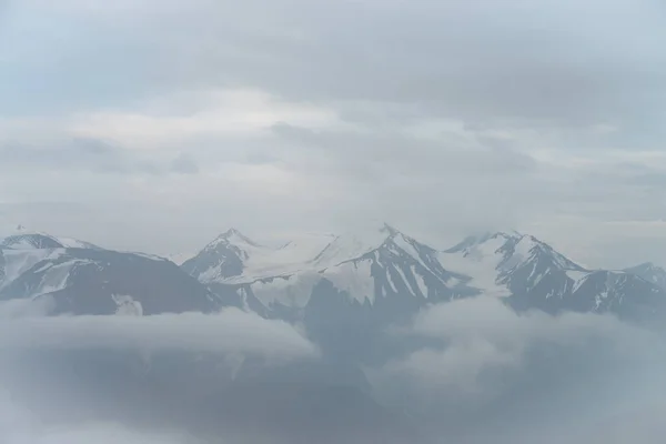 低雲の上に3つの大きな雪の山の峰と素晴らしいミニマリストの風景 曇り空に大きな雪の山の頂上と大気ミニマリズム 素晴らしい雪の山への印象的な眺め — ストック写真