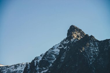 Atmosferik dağ manzarası. Siyah dağ silueti. Güneş ışığında karlı, keskin kayalık bir tepe noktası. Alp manzaralı, karla kaplı dağ tepede, mavi gökyüzünün altında gün ışığıyla tepede.