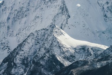 Karla kaplı dev dağ duvarının arka planında zirveye ulaşmış büyük kar kayalarıyla muhteşem bir dağ manzarası. Güneş ışığında karlı dağların olduğu atmosferik bir manzara. Büyük karlı dağlar