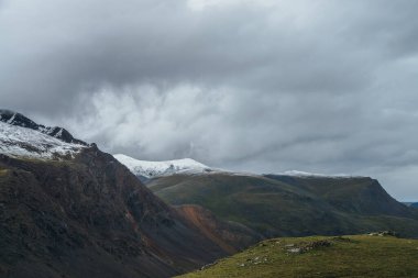 Atmosferik alp manzarası derin vadi ve karla kaplı çok renkli dağlarla bulutlu havada. Bulutlu gökyüzünün altında karla kaplı sıradağlarla güzel bir manzara. Karlı Motley yüksek dağları
