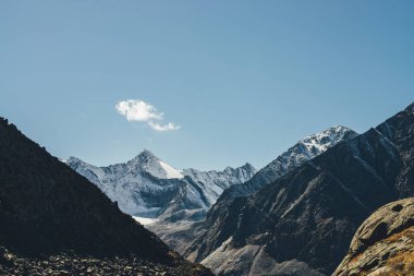 Yüksek karlı dağları olan dağlık bir arazi. Gökyüzünde sirrus bulutlarının altında zirveye ulaşmış. Güneş ışığıyla kaplı dağlara atmosferik bir manzara. Siyah kayalar ve beyaz kar, gün ışığında sivri tepeler..