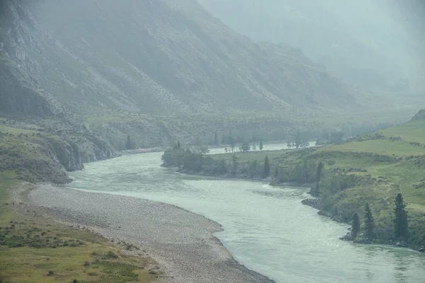 Geniş dağ nehri olan güzel sisli dağ manzarası. Koyu yeşil kasvetli manzara ve sisli dağ nehri. Yağmurlu havada, büyük dağların arasındaki büyük nehrin karanlık atmosferik görüntüsü.