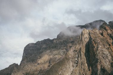 Görünüşte dağ manzarası, bulutlu gökyüzünde harika kayalar, klasik renklerde. Muhteşem güneşli manzara, alçak bulutlar kayalık dağın tepesinde pastel tonlarda. Güneş ışığı ve alçak bulutlarda güzel kahverengi kaya
