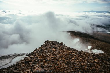 Dağların tepesinde atmosferik manzara, kalın alçak bulutların üzerinde kar var. Uçurumun kenarından bulutların üzerinden minimalist görüş. Yoğun bulutlar üzerinde dağ sırası olan güzel, minimum alp manzarası.