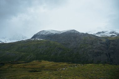 Karlı dağlarla kaplı minimalist dağlarda alçak bulutlar ve bulutlu hava. Düşük bulutlu gökyüzünün altındaki karlı dağ sırasının arka planında derin bir vadi. Yüksek dağlarda atmosfer minimalizmi.