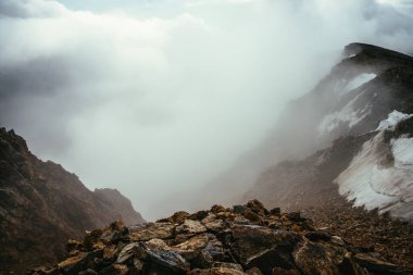Dağların tepesinde atmosferik manzara, kalın alçak bulutların üzerinde kar var. Uçurumun kenarından bulutların üzerinden minimalist görüş. Yoğun bulutlar üzerinde dağ sırası olan güzel, minimum alp manzarası.