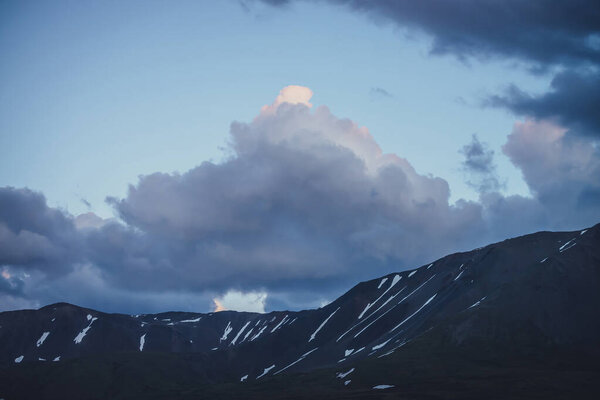 Beautiful violet rocky mountains with snow under dusk cloudy sky. Atmospheric sunset mountain scenery. Awesome rocks under purple clouds in blue sunrise sky. Twilight sky. Evening mountain landscape.