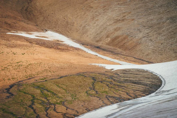 Sunny mountain desert relief with long glacier on slope in sunlight. Scenic highlands landscape with small glacier on mountainside and melt water streams high in mountains. Highland desert scenery.