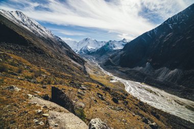 Büyük karlı dağları ve dağlık nehri olan güzel bir dağ manzarası. Sonbahar renklerinde kayaların arasında vadide birçok dere var. Gün ışığında. Sonbaharda yüksek kar duvarı olan güneşli bir manzara.
