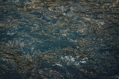 Güneşin doğuşunda ya da batışında dağ gölünün altın suyunun atmosferik arka planı. Su yüzeyinin altın güneş ışığını yansıtan manzaralı bir parçası. Güneş ışığı altın mavisi su deresine yansıyor..