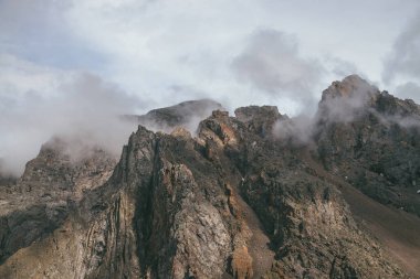 Görünüşte dağ manzarası, bulutlu gökyüzünde harika kayalar, klasik renklerde. Muhteşem güneşli manzara, alçak bulutlar kayalık dağın tepesinde pastel tonlarda. Güneş ışığı ve alçak bulutlarda güzel kahverengi kaya