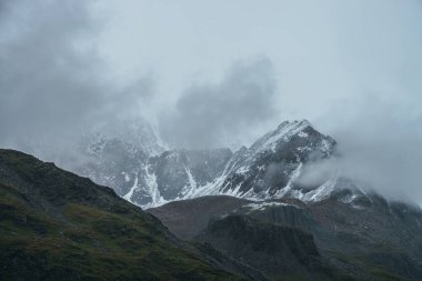 Atmosferik dağ manzarası alçak bulutlarda karla kaplı. Bulutlu havada keskin zirvesi olan dramatik dağ manzarası. Bulutlu gökyüzünde karlı, sivri tepeye müthiş bir manzara.