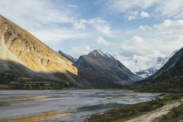 stock image Scenic landscape with footpath along water streams in valley in autumn colors with view to snowy mountains and rocks in golden sunshine. Colorful autumn scenery with mountain creek and snowy mountains