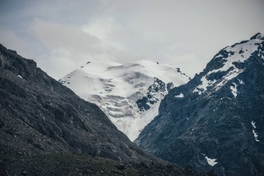 Bulutlu gökyüzünde harika karlı dağ manzarası. Atmosferik bulutlu, yüksek dağlı ve buzullu bir manzara. Karlı büyük dağlar. Bulutlarda güzel karlı dağlar.
