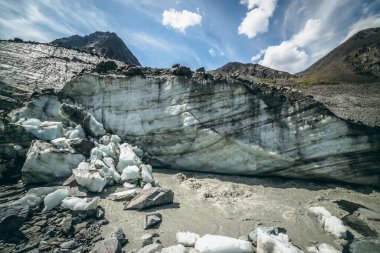 Buzuldan başlayan dağ nehri ile yüksek dağın arka planındaki geniş morinalar arasında manzaralı dağlık araziler. Dağ nehri ve kaya zirvesinin kaynağında buzullu güzel bir manzara..