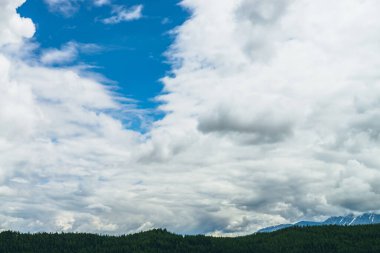 Mavi gökyüzünde güzel bulutlarla manzaralı doğa manzarası. Karlı dağların ve ormanın üzerindeki bulutlarla dolu renkli bulutlar. Beyaz bulutlu gökyüzünün doğası. Doğal bulutlu gökyüzü arkaplanı.