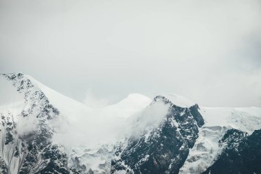Atmosferik dağlar alçak bulutlarda kar kornişleri olan büyük karlı dağ tepeleriyle kaplı. Bulutlu havada kar beyazı yüksek zirvesiyle muhteşem bir manzara. Bulutlardaki dev dağ duvarı.
