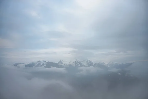 低雲の上に3つの大きな雪の山の峰と素晴らしいミニマリストの風景 曇り空に大きな雪の山の頂上と大気ミニマリズム 素晴らしい雪の山への印象的な眺め — ストック写真