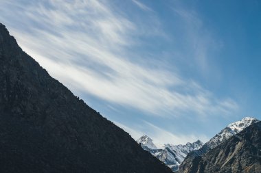 Yüksek karlı dağları olan dağlık bir arazi. Gökyüzünde sirrus bulutlarının altında zirveye ulaşmış. Güneş ışığıyla kaplı dağlara atmosferik bir manzara. Siyah kayalar ve beyaz kar, gün ışığında sivri tepeler..