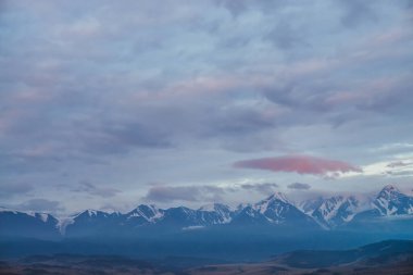 Leylak bulutlarının altında karlı dağ sıralarının olduğu manzaralı şafak manzarası. Gün batımında ya da gün doğumunda mavi bulutlu gökyüzünün altında karlı yüksek dağ sırtı olan atmosferik alp manzarası.