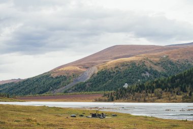 Dağ gölü manzaralı kamp ateşi ve sonbahar renklerinde ormanlı karışık dağlar. Sığ gölü ve çok renkli tepeleri olan manzaralı sonbahar manzarası. Güzel sonbahar dağ manzarası.
