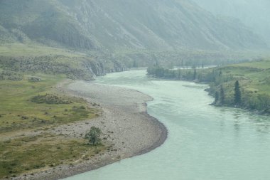 Geniş dağ nehri olan güzel sisli dağ manzarası. Koyu yeşil kasvetli manzara ve sisli dağ nehri. Yağmurlu havada, büyük dağların arasındaki büyük nehrin karanlık atmosferik görüntüsü.