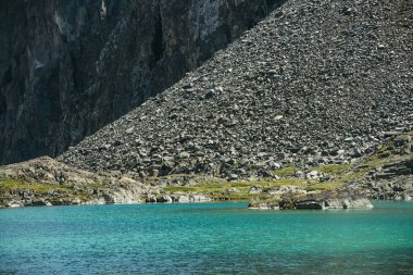 Turkuaz dağ gölü olan güzel manzaralı bir yer. Güneş ışığında gök mavisi bir buzul gölü. Büyük kayalık dağın yakınındaki dağ gölünün berrak su yüzeyine sahip renkli güneşli bir manzara. Buzul Gölü.