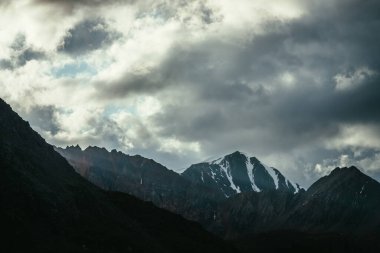 Atmosferik dağ manzarası. Kayalardan oluşan siluetler ve bulutlu gökyüzünün altında karla kaplı keskin tepeler. Karlı büyük kayalar. Tepesi karla kaplı güzel bir dağ manzarası. Karla kaplı sivri uç.