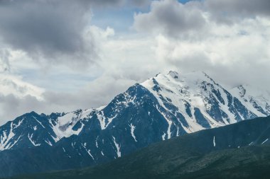 Mavi gökyüzündeki beyaz bulutlar arasında yüksek karlı dağ sıraları olan muhteşem dağlar. Bulutlu havada, kar beyazı dağ sırtı olan atmosferik dağ manzarası. Harika kar zirvesi
