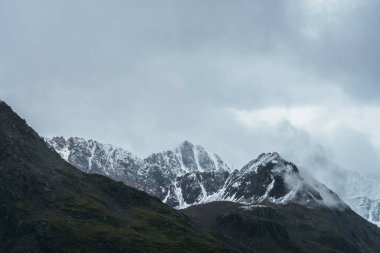 Atmosferik dağ manzarası alçak bulutlarda karla kaplı. Bulutlu havada keskin zirvesi olan dramatik dağ manzarası. Bulutlu gökyüzünde karlı, sivri tepeye müthiş bir manzara.