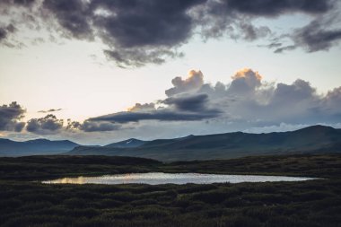 Canlı turuncu gradyan gökyüzü altında göl manzaralı gün batımı manzarası. Renkli dağ gündoğumu manzarası bulutlu gökyüzünde aydınlatıcı bir renk ve gölün altın yansıması. Şafak vakti yükselen bulutlar.