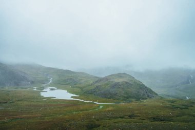 Atmosferik alp manzarası yağmur sırasında tepelerin arasındaki güzel dağ gölü. Yüksek dağlarda kar yağışı olan manzara. Yağmurlu havada dağlık arazide alçak bulutlar. Bulutlu dağ manzarası.