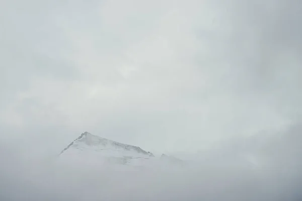 雲の中に高点岩と最小限の山の風景 雲の上に鋭い雪の山のピークとミニマリストの山の風景 雪は白い雲の上に白い頂点を指摘した 濃い霧の中で大きなトップ — ストック写真
