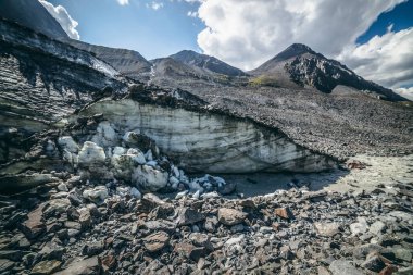 Buzuldan başlayan dağ nehri ile yüksek dağın arka planındaki geniş morinalar arasında manzaralı dağlık araziler. Dağ nehri ve kaya zirvesinin kaynağında buzullu güzel bir manzara..